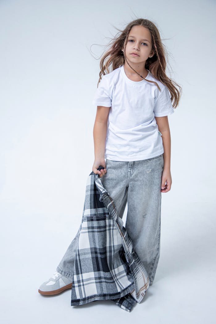 Young girl in white tee and jeans holding plaid shirt in bright studio.